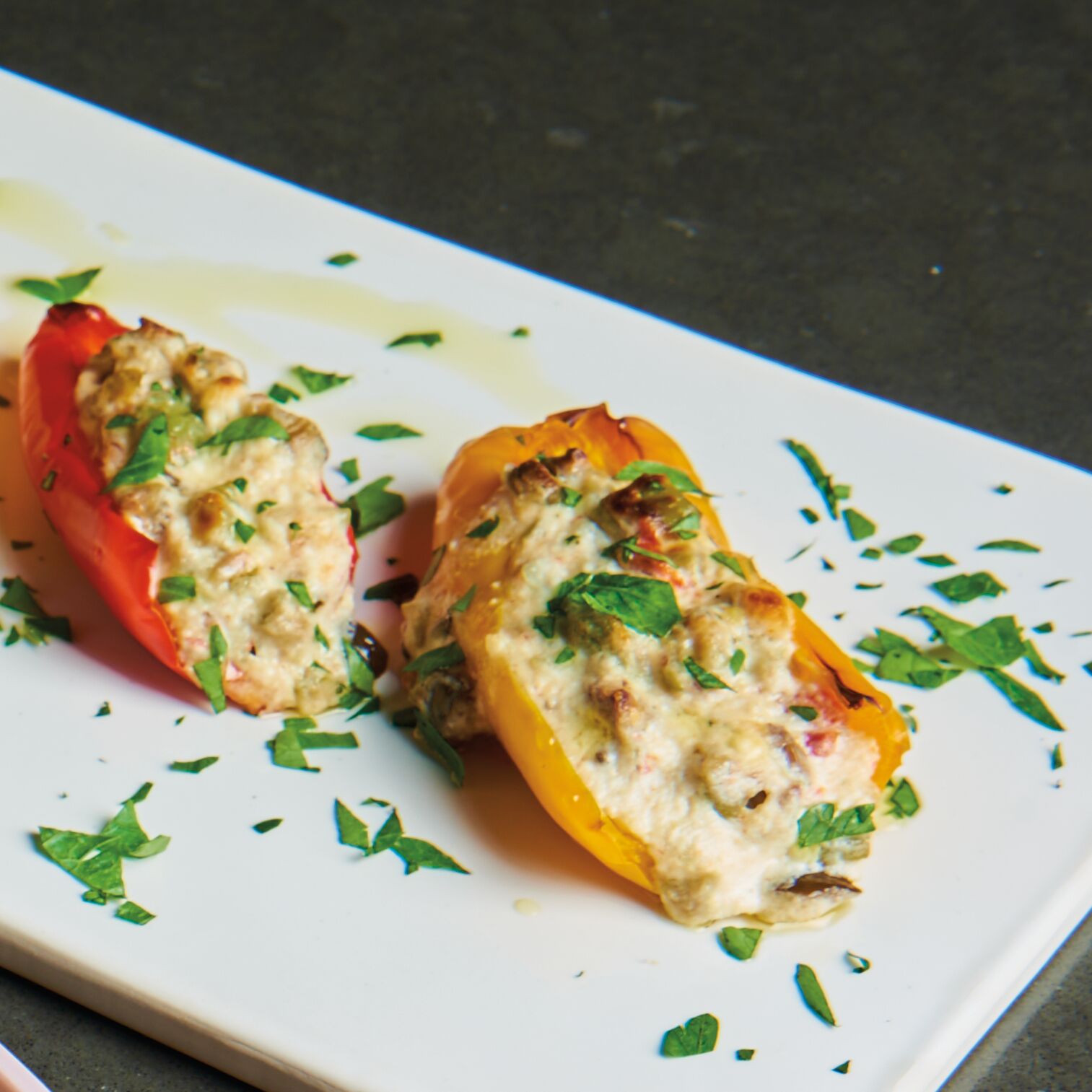 Red and yellow mini bell peppers stuffed with ricotta and olive tapenade mixture, garnished with chopped parsley on a white rectangular plate