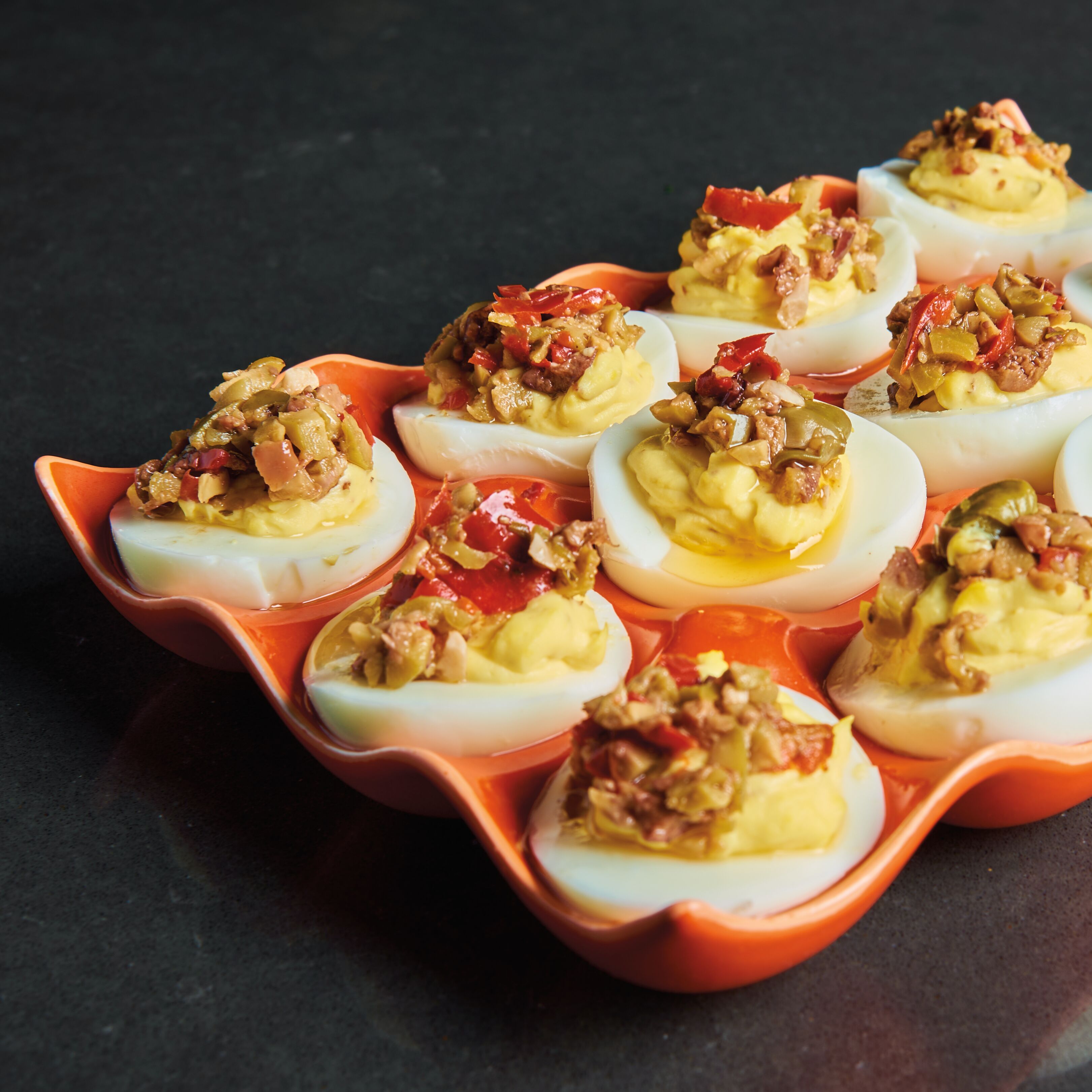 Deviled eggs stuffed with chopped olive tapenade on an orange dish