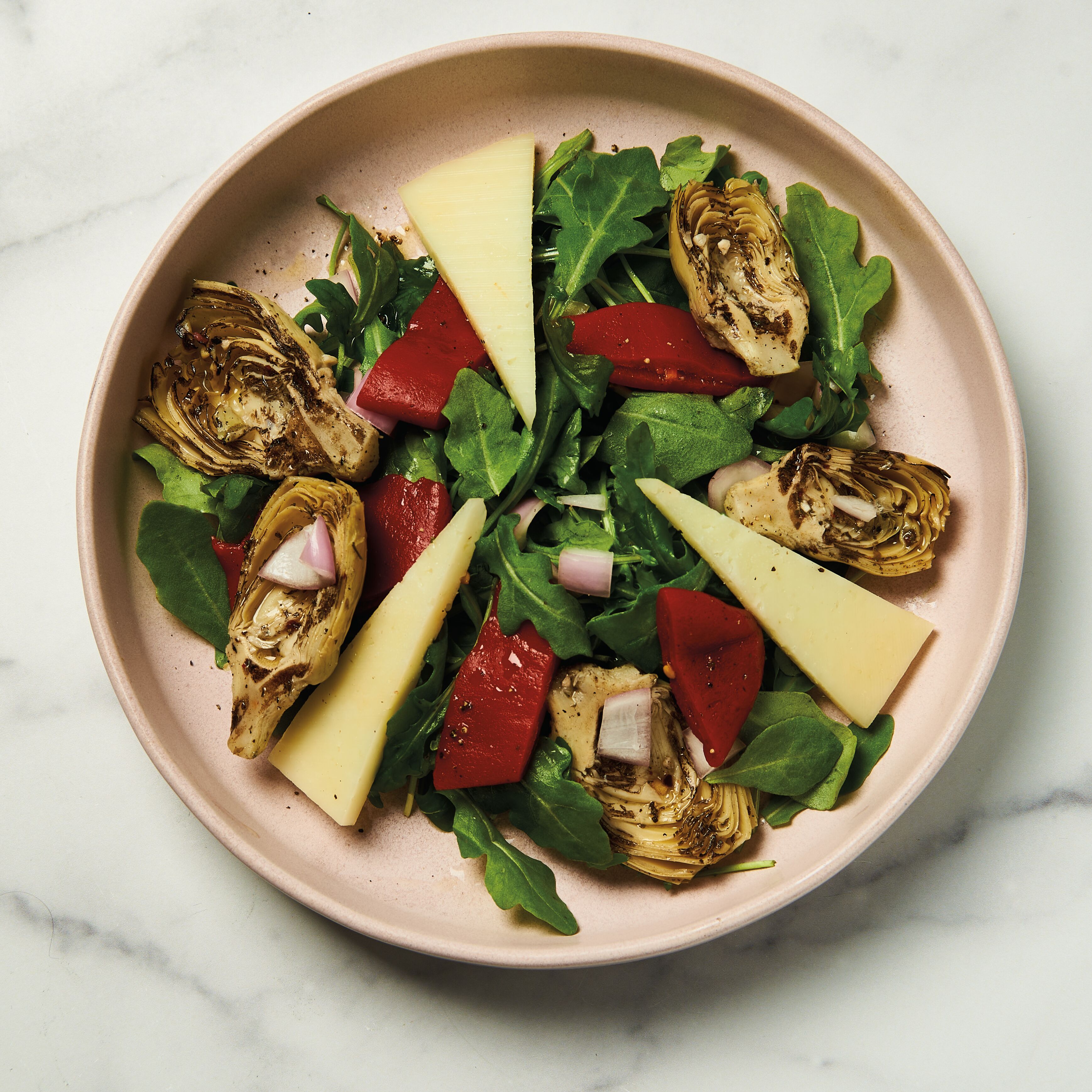 Arugula, roasted red piquillo peppers, grilled artichoke halves, manchego slices, and shallots arranged on a salad plate