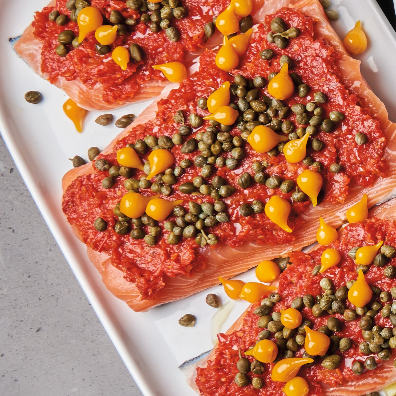 salmon fillets topped with roasted tomato spread, capers, and red peruvian pearl peppers
